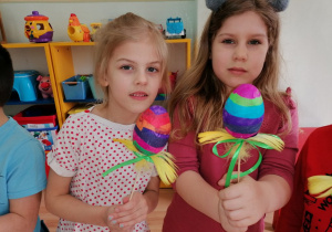 Dziewczynki pokazują wykonane pisanki - jajka akrylowe oklejane kolorowymi paskami bibuły.